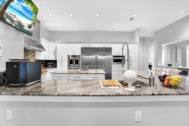 kitchen with built in fridge, white cabinets, light stone counters, and kitchen peninsula