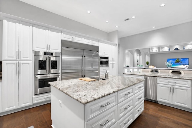 kitchen with a kitchen island, white cabinetry, light stone counters, stainless steel appliances, and dark wood-type flooring