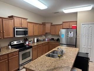 kitchen featuring sink, an island with sink, light stone counters, and stainless steel appliances