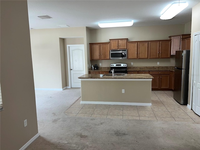 kitchen featuring appliances with stainless steel finishes, sink, light colored carpet, dark stone counters, and a center island with sink