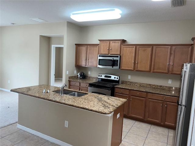 kitchen with stone countertops, appliances with stainless steel finishes, sink, light tile patterned flooring, and a center island with sink