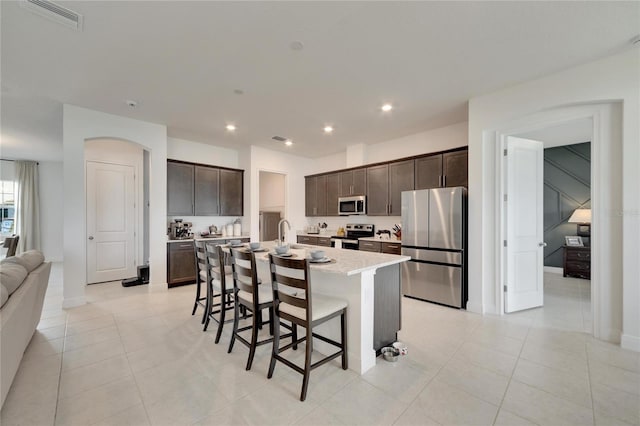 kitchen with stainless steel appliances, a kitchen bar, an island with sink, and light tile flooring