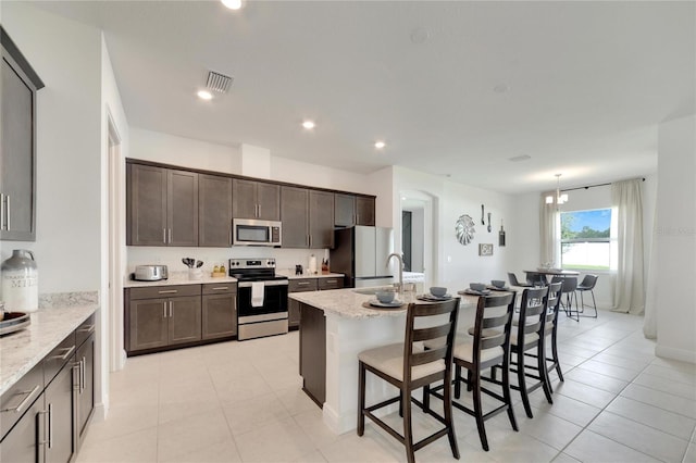 kitchen featuring appliances with stainless steel finishes, light stone counters, a breakfast bar area, and a center island with sink