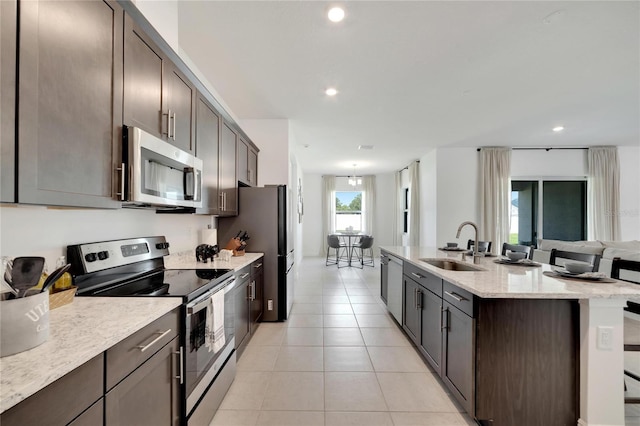 kitchen with stainless steel appliances, light stone countertops, dark brown cabinets, sink, and light tile floors