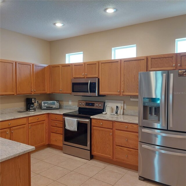 kitchen with light stone counters, a textured ceiling, stainless steel appliances, and light tile patterned flooring