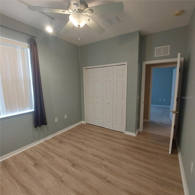 unfurnished bedroom featuring ceiling fan, rail lighting, a closet, and light wood-type flooring