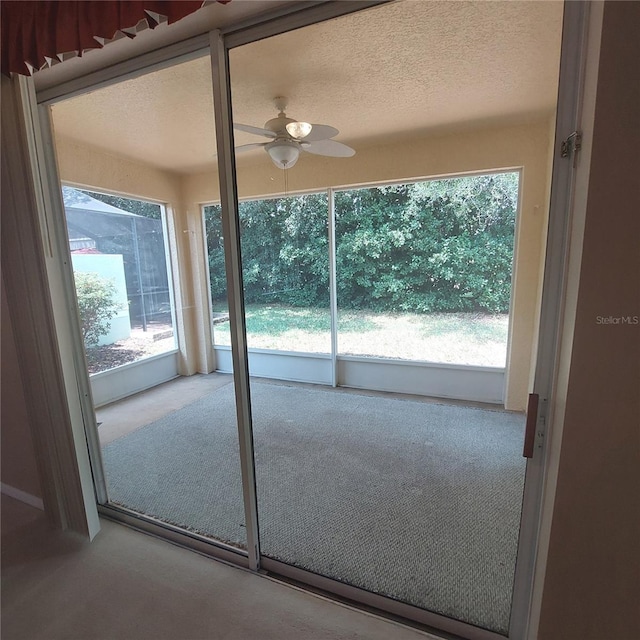 doorway with a textured ceiling, ceiling fan, and carpet flooring