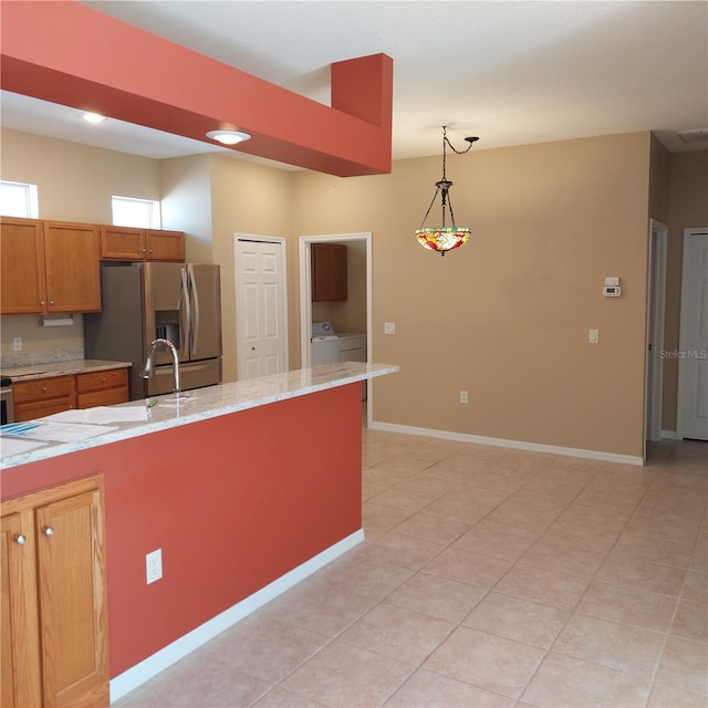 kitchen with stainless steel refrigerator with ice dispenser, light stone counters, pendant lighting, and washer and clothes dryer