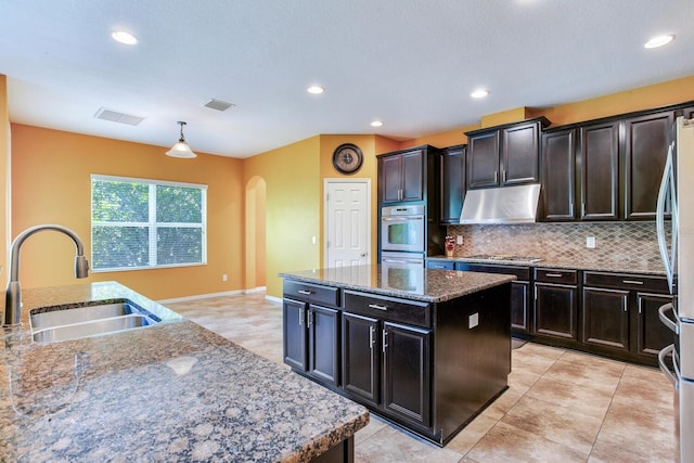 kitchen featuring a center island with sink, tasteful backsplash, dark stone counters, sink, and light tile floors