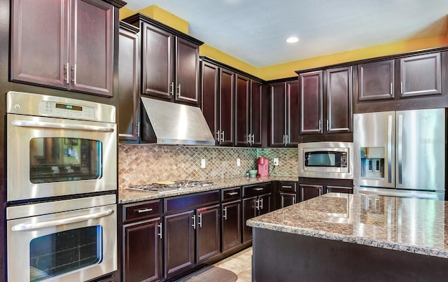 kitchen with appliances with stainless steel finishes, light tile floors, backsplash, dark brown cabinets, and light stone countertops