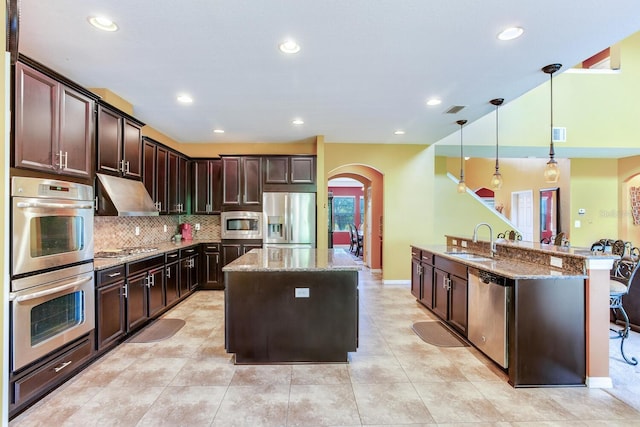 kitchen featuring appliances with stainless steel finishes, wall chimney exhaust hood, hanging light fixtures, kitchen peninsula, and stone counters