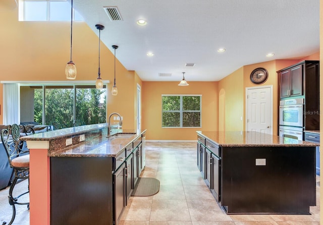 kitchen featuring a kitchen breakfast bar, a kitchen island with sink, decorative light fixtures, light tile flooring, and sink