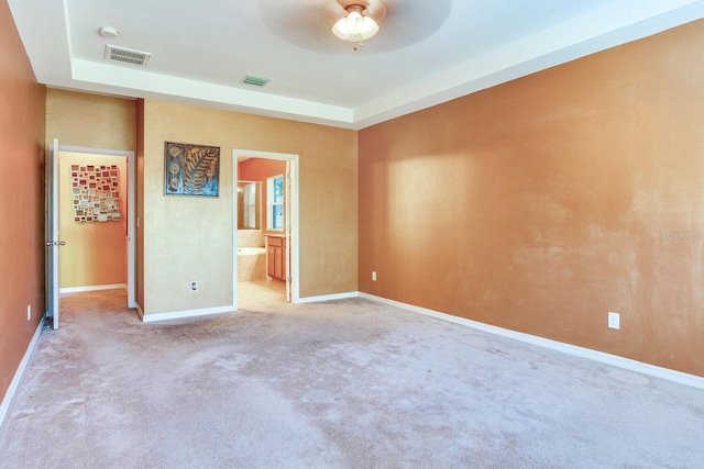 unfurnished bedroom featuring a tray ceiling, light colored carpet, ceiling fan, and ensuite bathroom