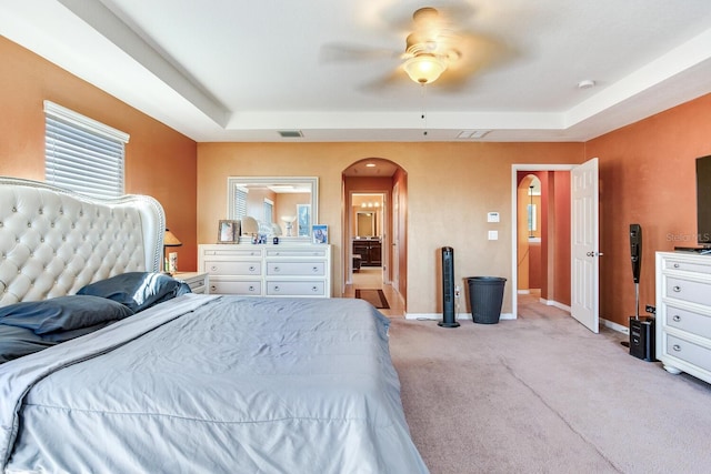 bedroom with light carpet, ceiling fan, and a raised ceiling