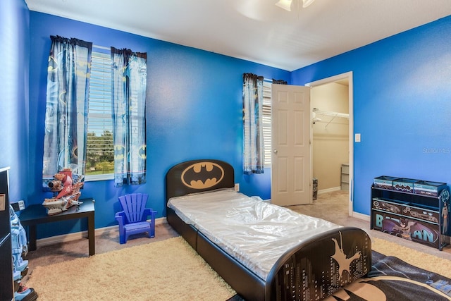 bedroom with a closet, ceiling fan, a walk in closet, and light carpet