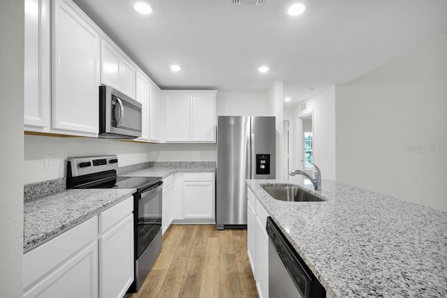 kitchen with sink, light stone counters, white cabinets, appliances with stainless steel finishes, and light hardwood / wood-style flooring