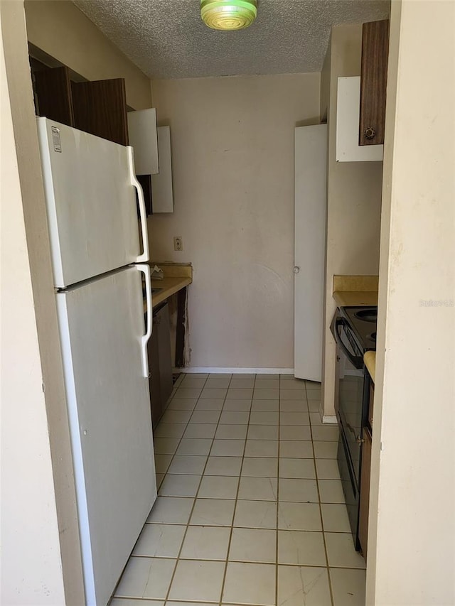 kitchen with light tile patterned floors, a textured ceiling, black range with electric stovetop, and white refrigerator