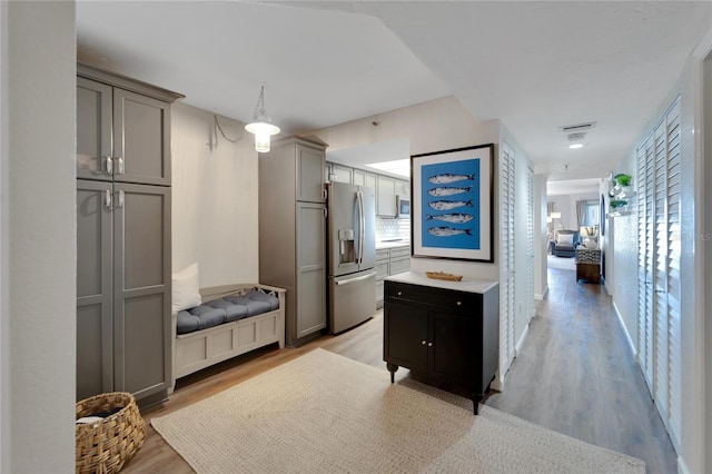 interior space featuring light hardwood / wood-style flooring, hanging light fixtures, and stainless steel refrigerator with ice dispenser