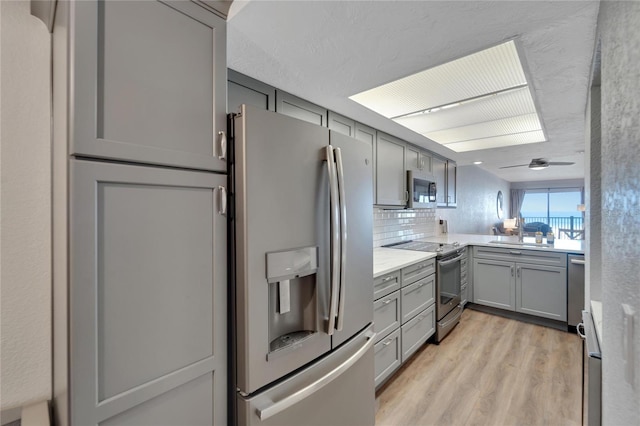 kitchen featuring appliances with stainless steel finishes, gray cabinets, ceiling fan, tasteful backsplash, and light wood-type flooring