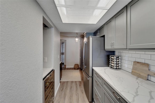 kitchen with beverage cooler, light stone counters, backsplash, light wood-type flooring, and gray cabinets