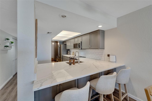 kitchen with backsplash, gray cabinets, a breakfast bar area, stainless steel appliances, and light hardwood / wood-style flooring