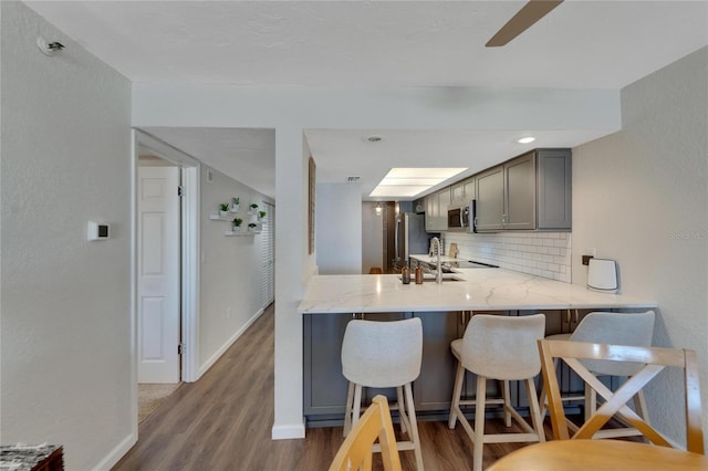 kitchen with tasteful backsplash, a breakfast bar area, stainless steel appliances, kitchen peninsula, and hardwood / wood-style flooring