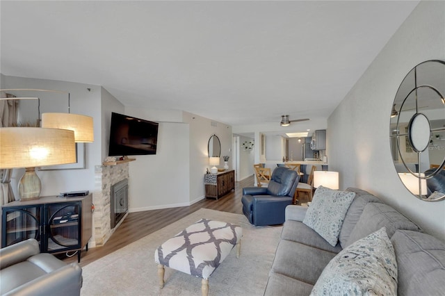 living room featuring hardwood / wood-style floors, ceiling fan, and a stone fireplace