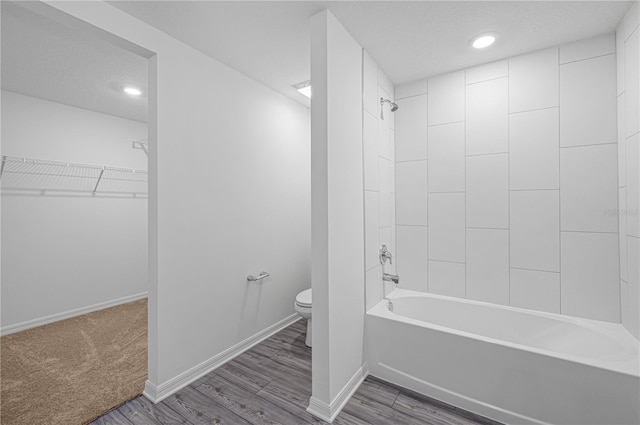 bathroom with toilet, hardwood / wood-style floors, tiled shower / bath combo, and a textured ceiling