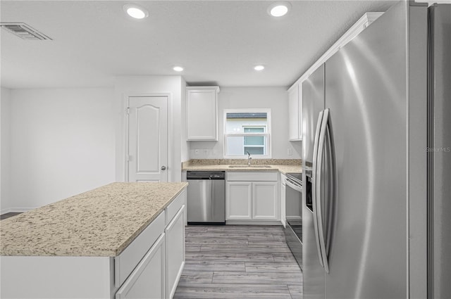 kitchen with white cabinetry, a center island, stainless steel appliances, and light hardwood / wood-style flooring