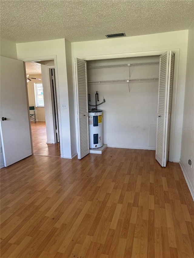 unfurnished bedroom featuring hardwood / wood-style floors, a textured ceiling, and electric water heater