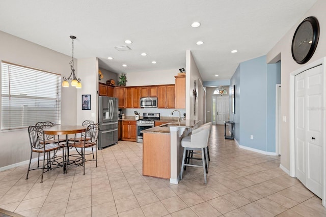 kitchen with kitchen peninsula, appliances with stainless steel finishes, a kitchen breakfast bar, decorative light fixtures, and a chandelier