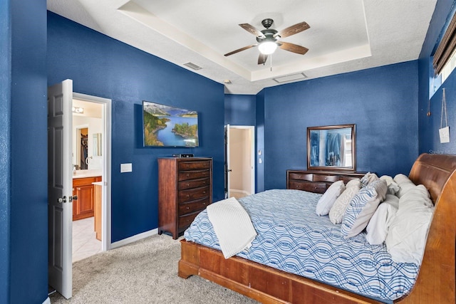 bedroom with a raised ceiling, ceiling fan, ensuite bathroom, and light carpet