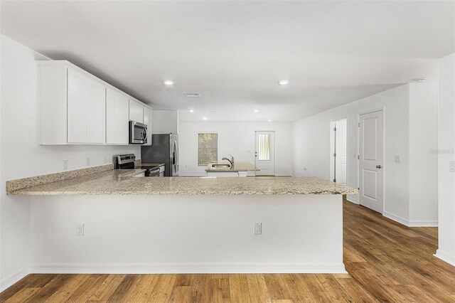 kitchen featuring kitchen peninsula, stainless steel appliances, sink, light hardwood / wood-style flooring, and white cabinets