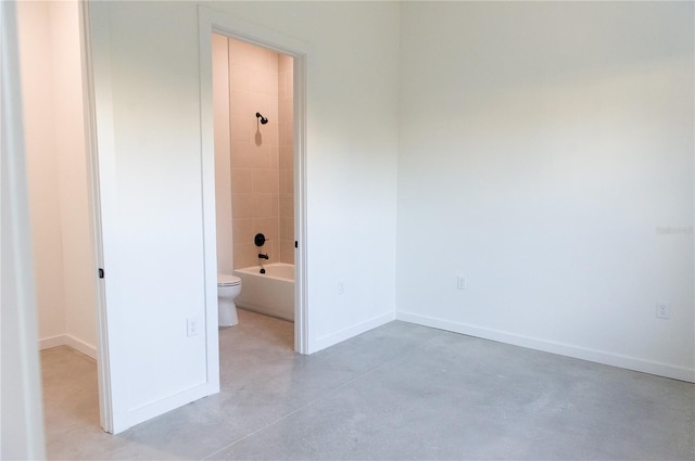 interior space with finished concrete flooring, baseboards, and connected bathroom