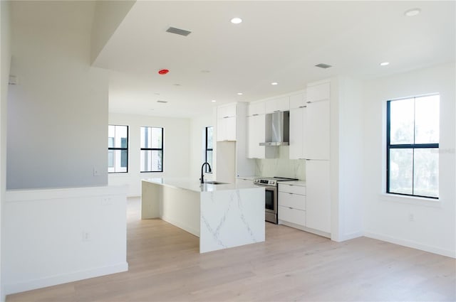 kitchen with wall chimney range hood, white cabinets, modern cabinets, electric stove, and a sink