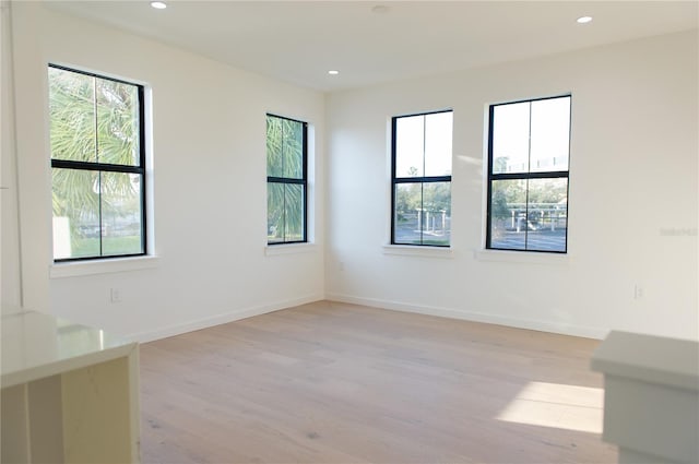 spare room featuring baseboards, light wood-type flooring, and plenty of natural light