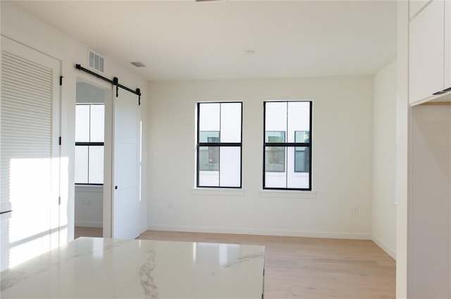 unfurnished room with visible vents, baseboards, light wood-type flooring, and a barn door