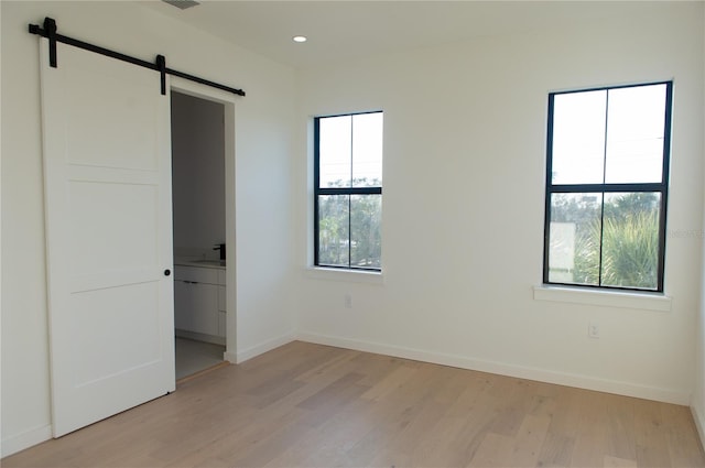 unfurnished bedroom with baseboards, multiple windows, a barn door, and light wood-style floors