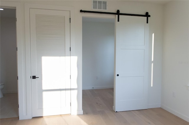 unfurnished bedroom featuring light wood-style flooring, baseboards, visible vents, and a barn door