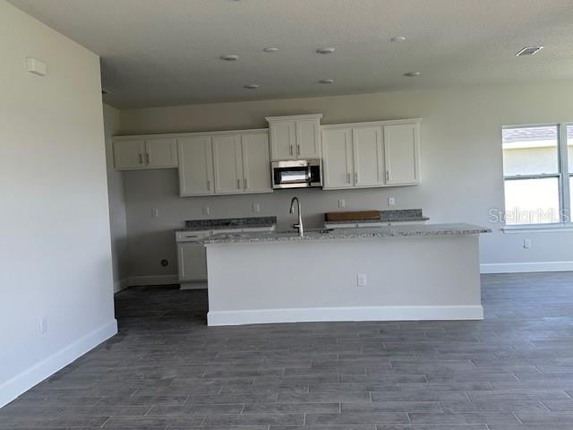 7002 162nd Pl E, Parrish, FL 34219 - kitchen with white cabinets, a kitchen island with sink, stainless steel microwave, dark wood-style flooring, and baseboards
