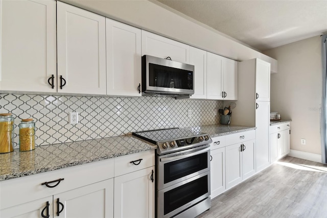 kitchen featuring light stone countertops, light hardwood / wood-style flooring, white cabinetry, backsplash, and appliances with stainless steel finishes