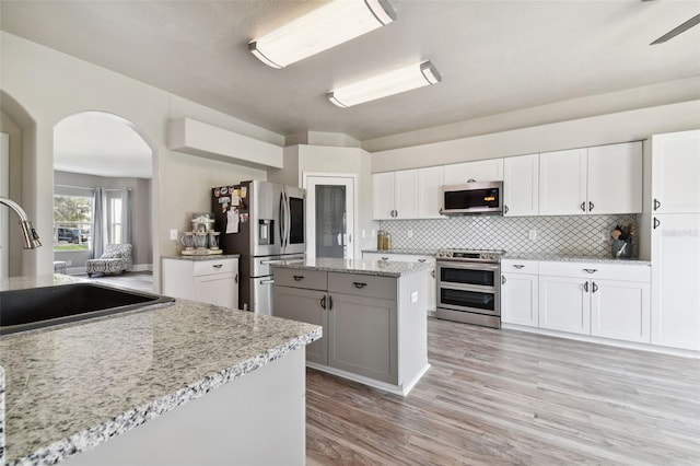 kitchen featuring light stone counters, white cabinets, light hardwood / wood-style floors, tasteful backsplash, and stainless steel appliances