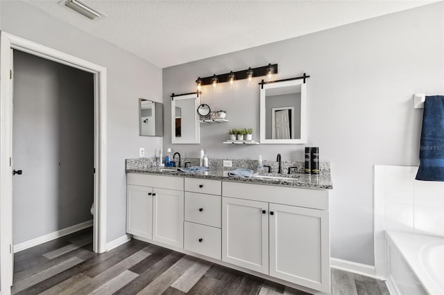 bathroom featuring hardwood / wood-style floors, double sink vanity, a tub, and a textured ceiling