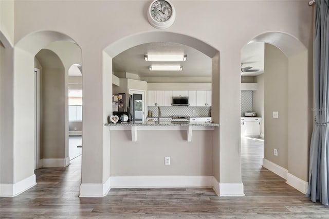 kitchen featuring white cabinets, tasteful backsplash, stainless steel appliances, hardwood / wood-style flooring, and light stone countertops