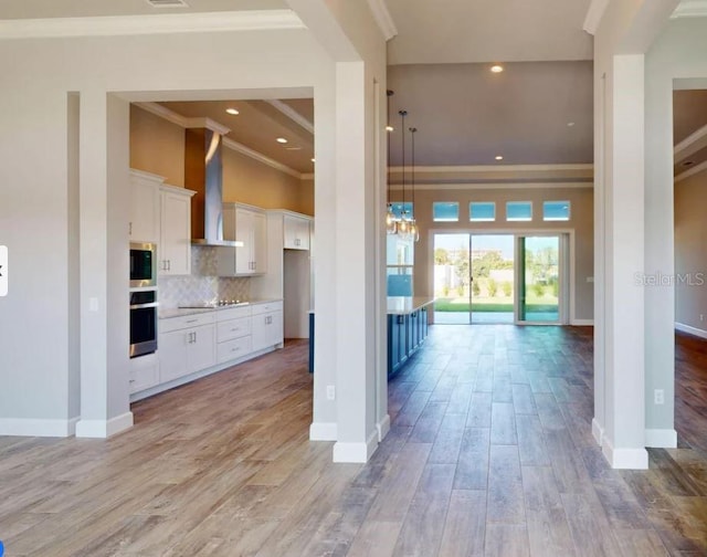 kitchen featuring white cabinets, wall chimney range hood, appliances with stainless steel finishes, tasteful backsplash, and light hardwood / wood-style floors