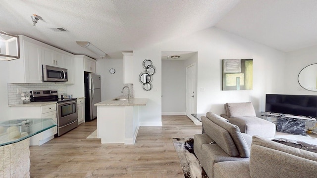 kitchen featuring a kitchen island with sink, white cabinets, stainless steel appliances, light stone countertops, and light wood-type flooring