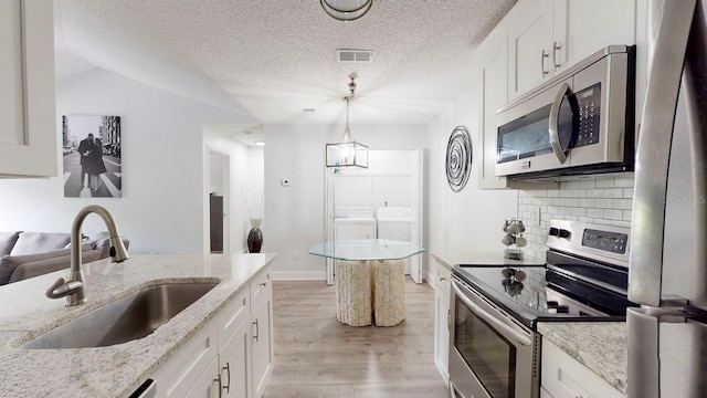 kitchen featuring sink, washer and clothes dryer, light hardwood / wood-style flooring, stainless steel appliances, and white cabinetry