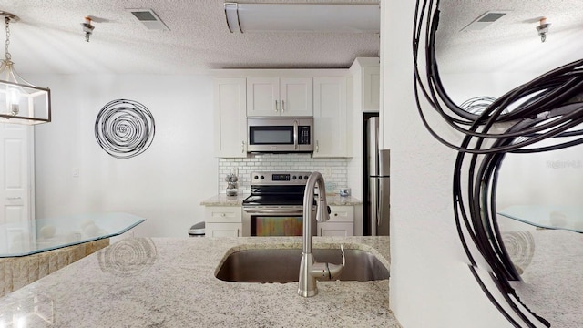 kitchen with white cabinets, appliances with stainless steel finishes, a textured ceiling, and tasteful backsplash