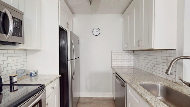 kitchen featuring a textured ceiling, appliances with stainless steel finishes, light stone countertops, and light hardwood / wood-style flooring