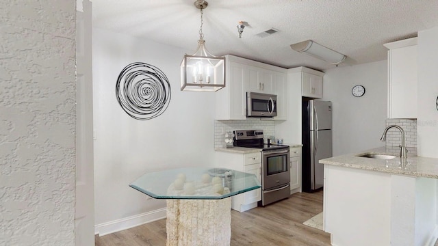 kitchen with hanging light fixtures, white cabinets, light hardwood / wood-style floors, stainless steel appliances, and tasteful backsplash